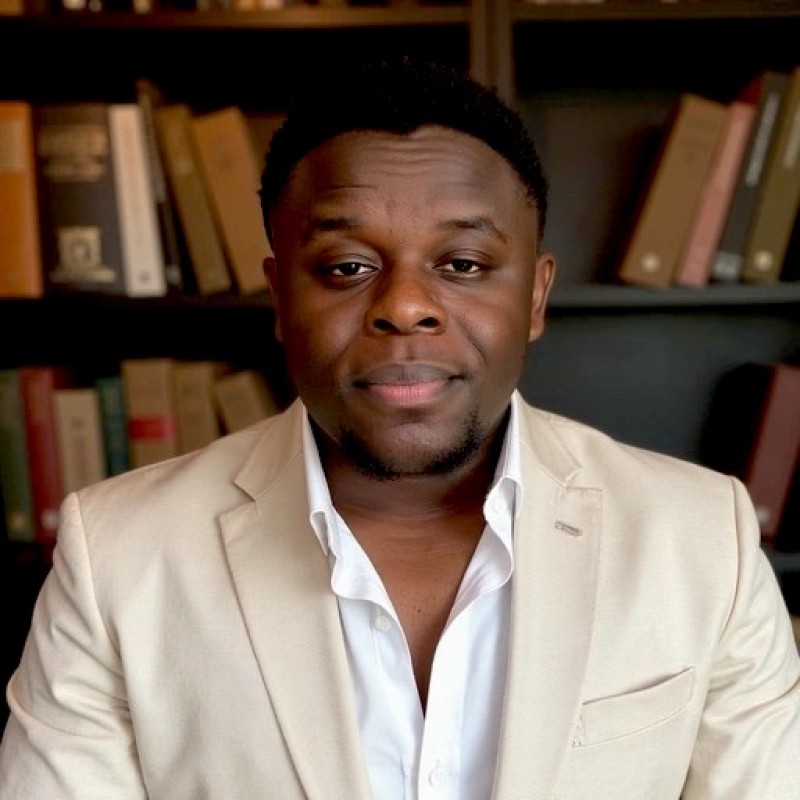 Gael Fokou Fobasso wearing a cream blazer, seated in front of a bookshelf